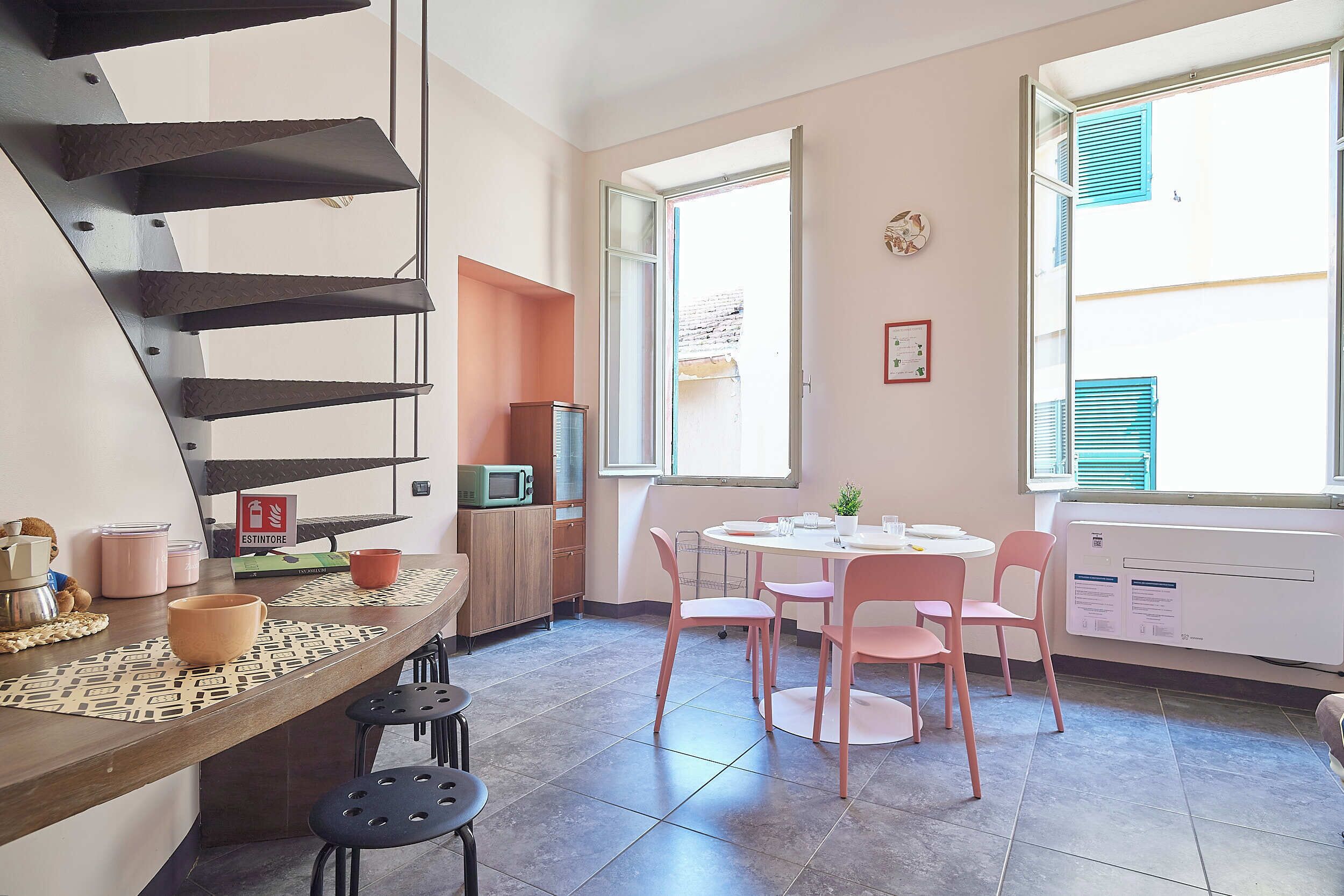Um espaço de estar compacto com cozinha compacta, área de jantar com cadeiras cor-de-rosa, mesa pequena e escada.