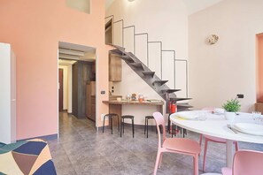 Eine moderne Küche mit eingebautem Herd, ein Essbereich mit rosa Stühlen und eine Treppe, die zu einer weiteren Ebene führt.