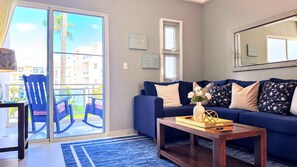 Ein Wohnzimmer mit einem blauen Sofa, einem Holztisch und Blick auf einen Balkon mit Gartenmöbeln.