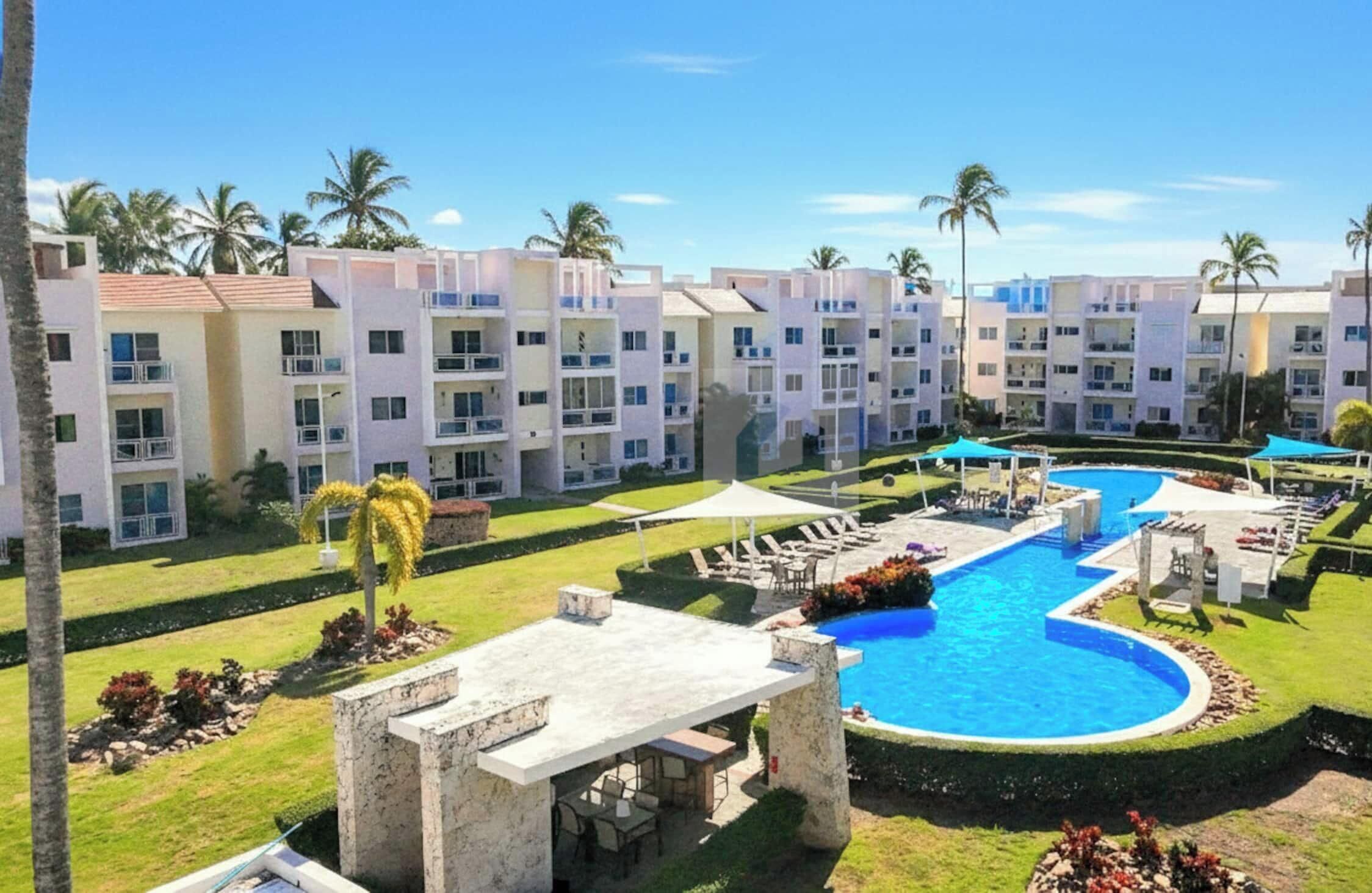 A hotel with a swimming pool, multiple balconies, and palm trees.