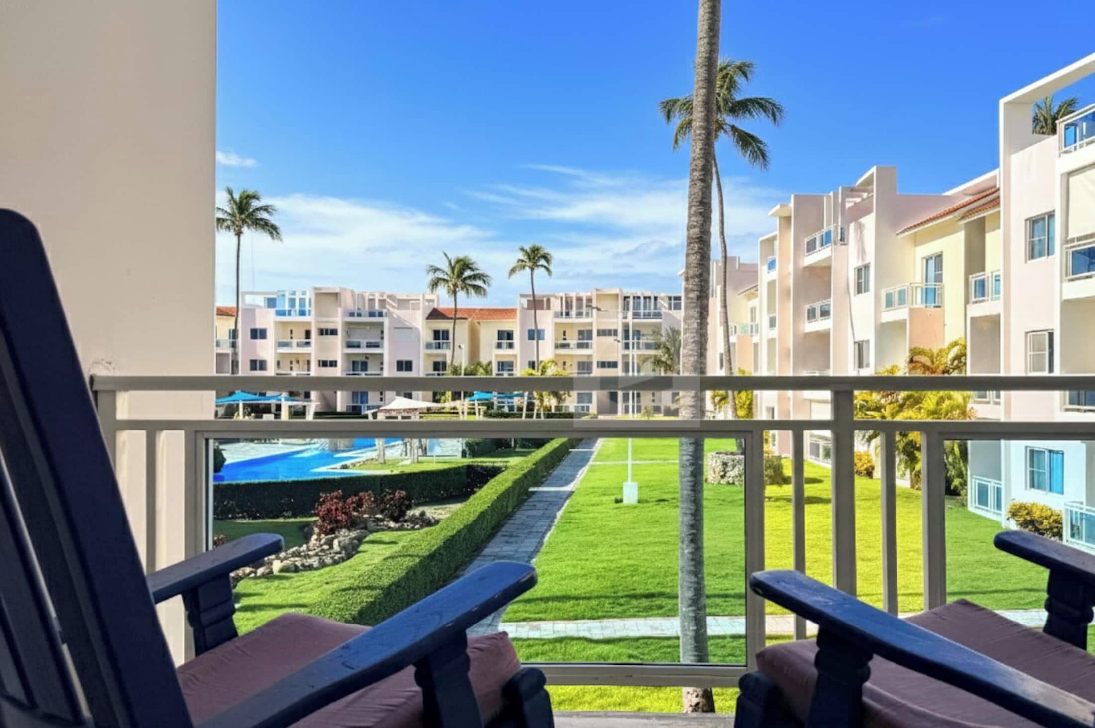 Un balcon avec deux chaises, une piscine et une vue sur un immeuble à plusieurs étages doté de balcons.