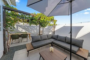 A modern outdoor seating area with a sectional sofa, a wooden table, and a pergola with climbing plants. - Luxury Apartment Nestled in Beautiful Natural Surroundings (Willemstad)