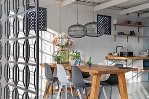 A modern kitchen with a wooden table, chairs, pendant lights, and a variety of kitchen appliances.