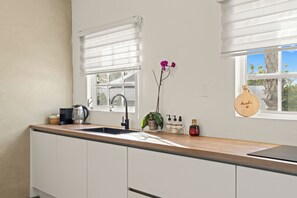 A modern kitchen with white cabinets, a wooden countertop, a coffee maker, a sink, and a window with a view of trees. - Luxury Apartment Nestled in Beautiful Natural Surroundings (Willemstad)