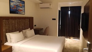 Habitación de hotel con una cama grande, un escritorio, equipo de aire acondicionado, televisor y un cuadro en la pared.