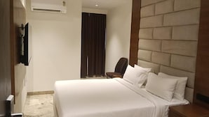 Habitación de hotel con una cama grande, cabecero de madera, televisor de pantalla plana montado en la pared y una mesita.