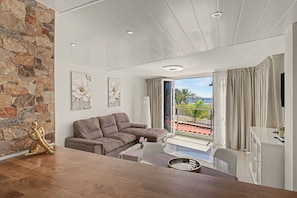 Una sala de estar moderna con una pared de piedra, un sofá modular, una mesa de comedor y vistas al exterior.