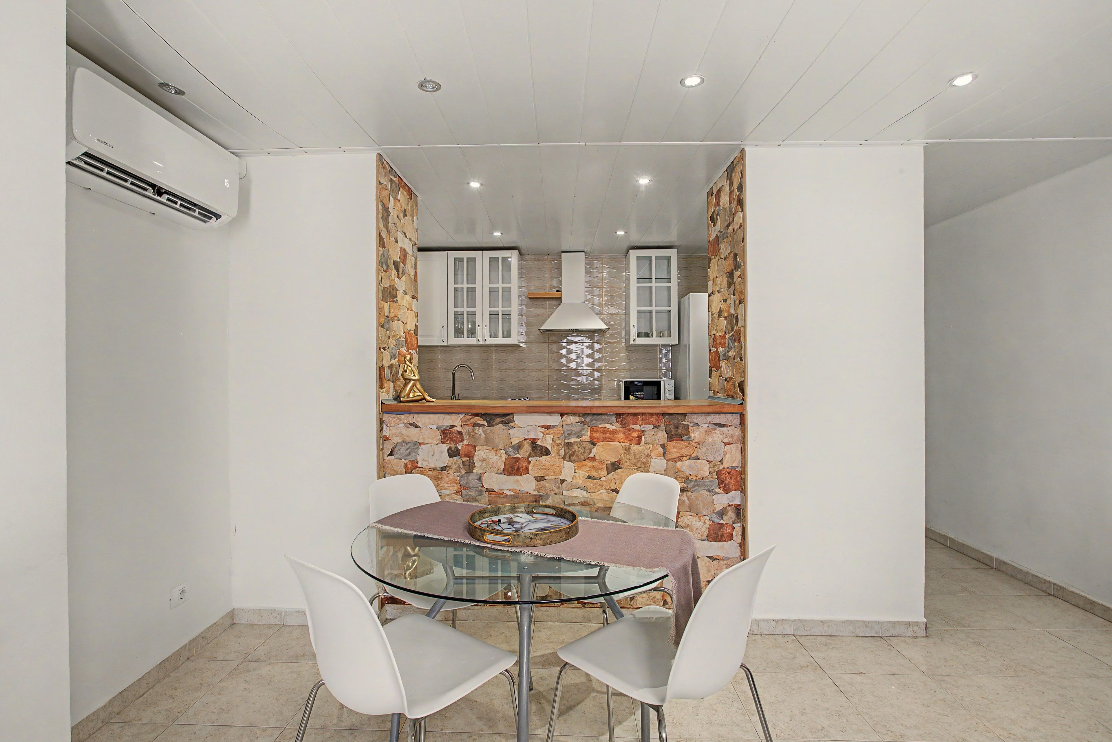 Una cocina compacta con detalles de piedra, una mesa de comedor de vidrio con sillas y un microondas en la encimera.