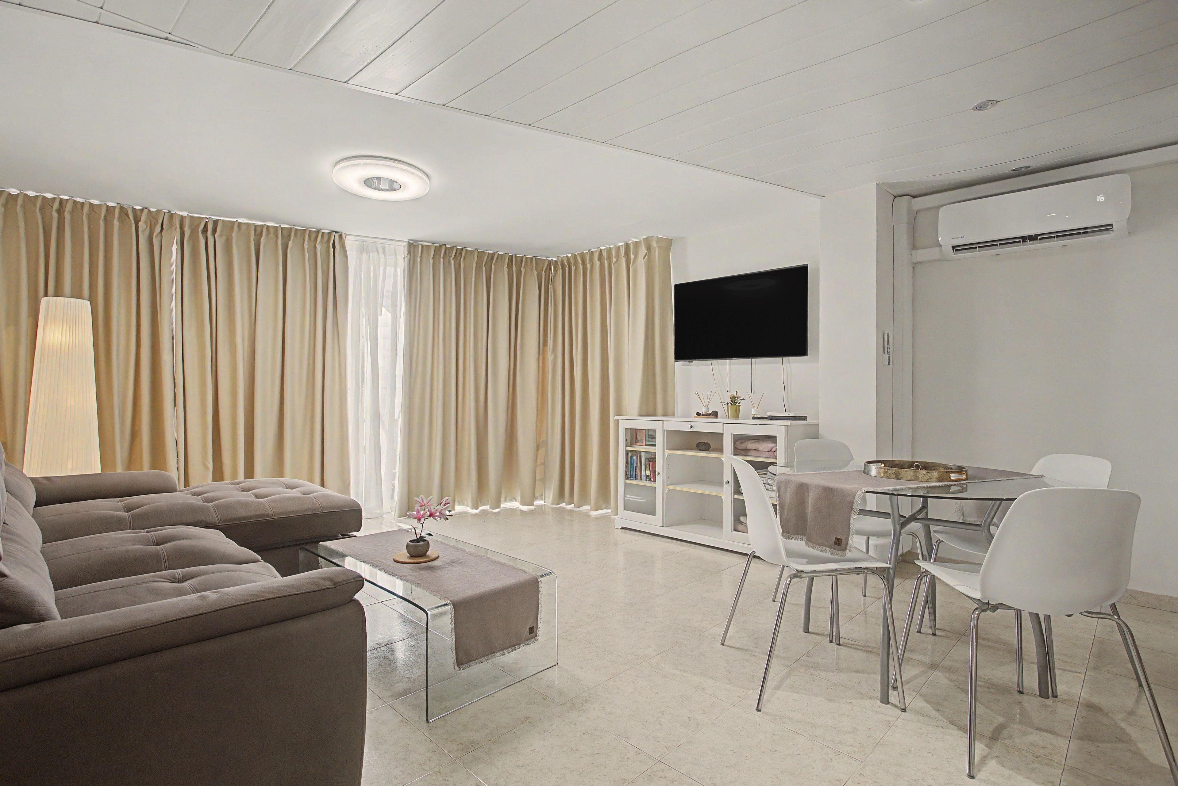 Una sala moderna con un sofá, una mesa de centro, un televisor y un comedor con sillas y una mesa.
