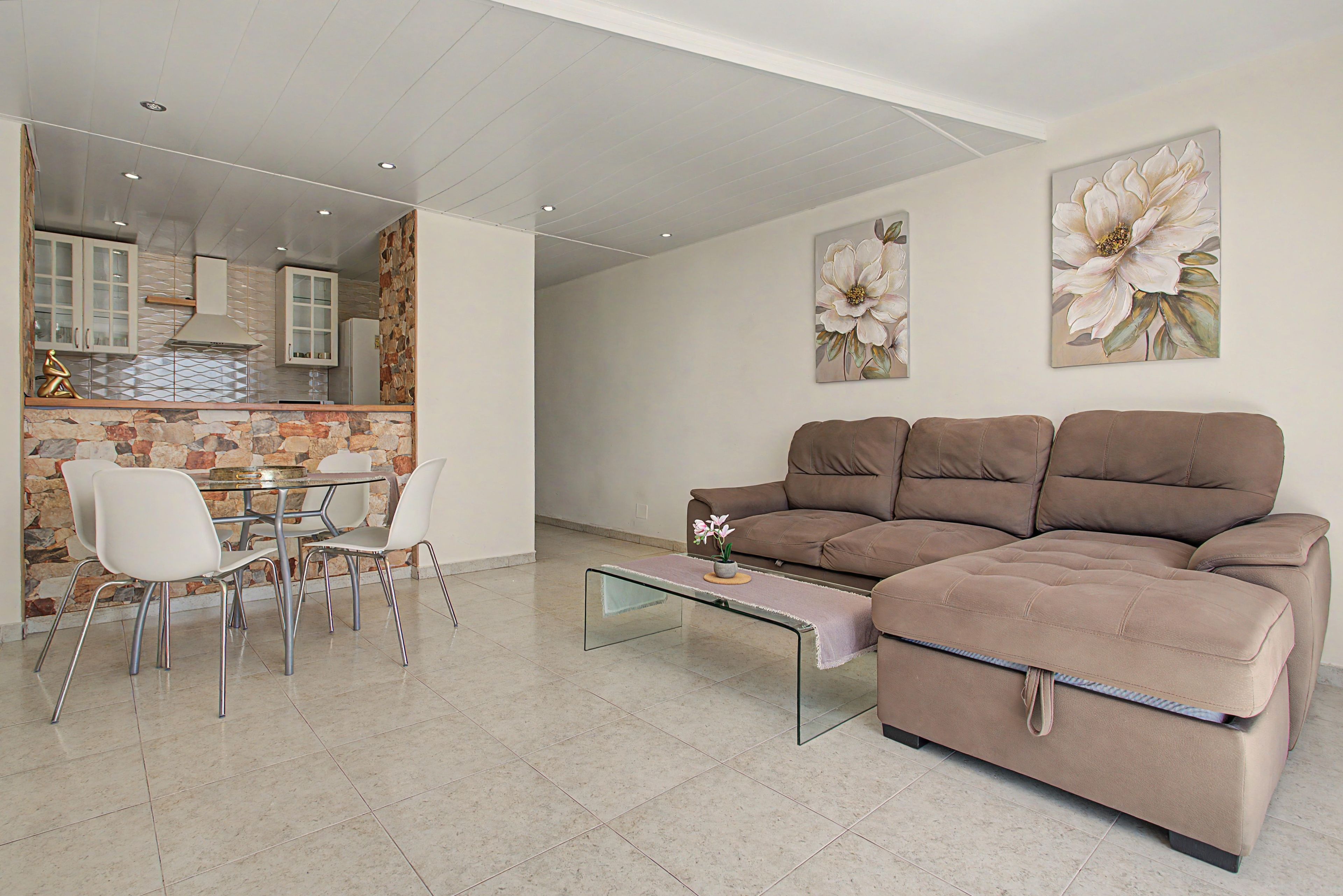 A modern living room with a sofa, a glass coffee table, and a dining area with chairs.