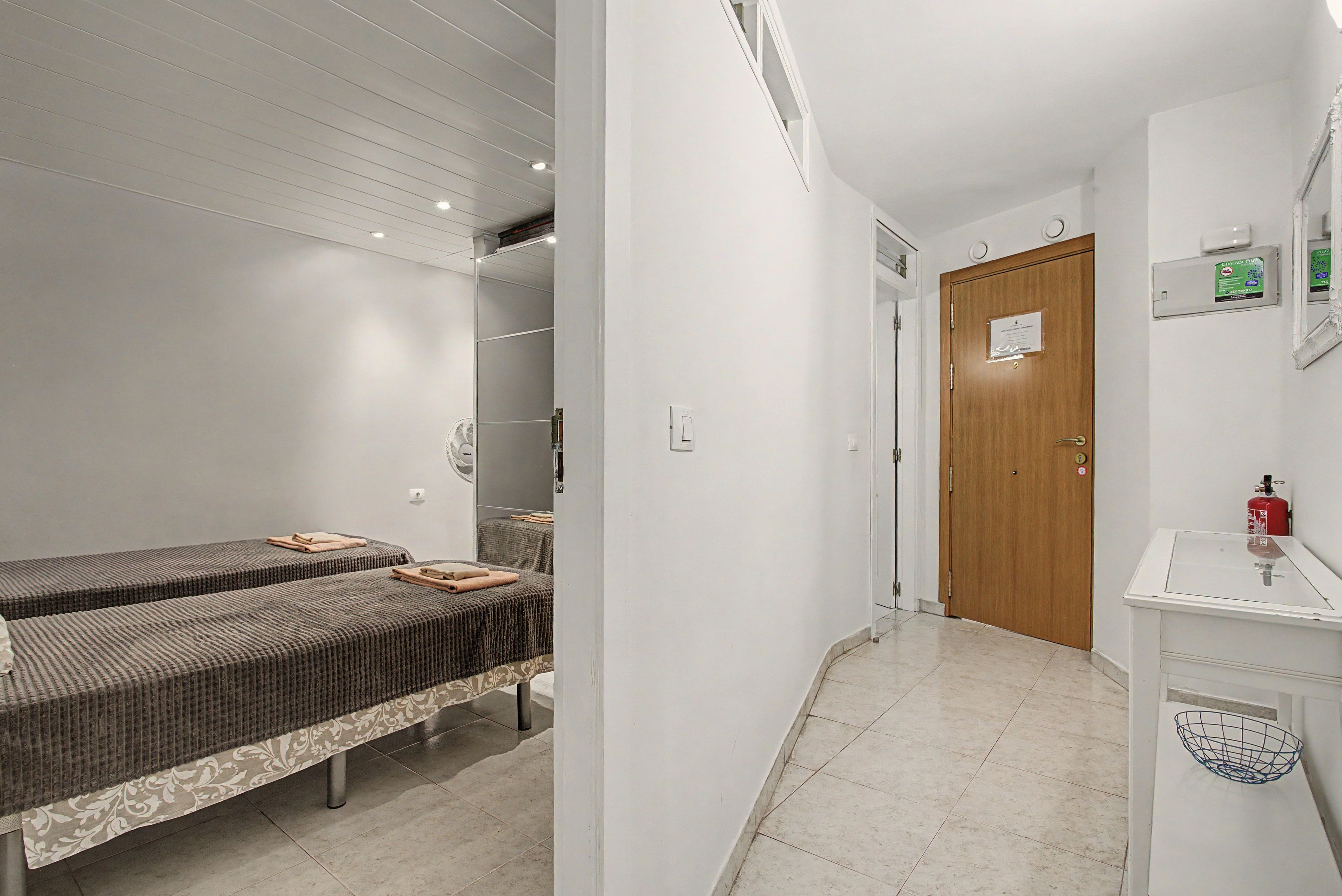 Ett hotellrum med två sängar, en trädörr, ett vitt handfat och en brandsläckare.