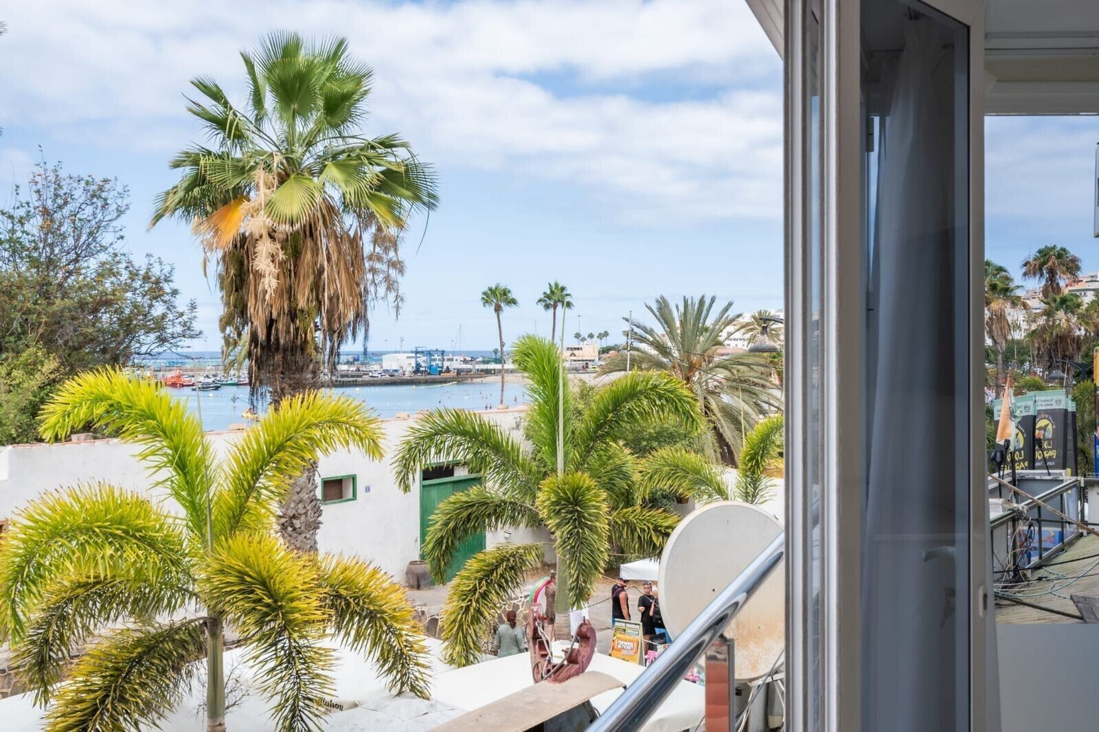 A balcony with a view of a marina, palm trees, and a building with a satellite dish.