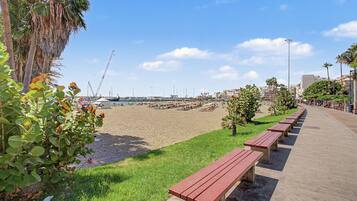 Een promenade aan het strand met banken, palmbomen en een helder uitzicht op het strand en gebouwen in de verte.