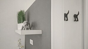 Una habitación minimalista con una pared gris, un estante blanco con una planta y una escultura, y una orquídea pequeña en el suelo.