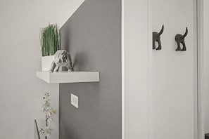 Ein schlicht eingerichteter Raum mit grauer Wand, einem weißen Regal mit Pflanze und Skulptur sowie einer kleinen Orchidee auf dem Boden.