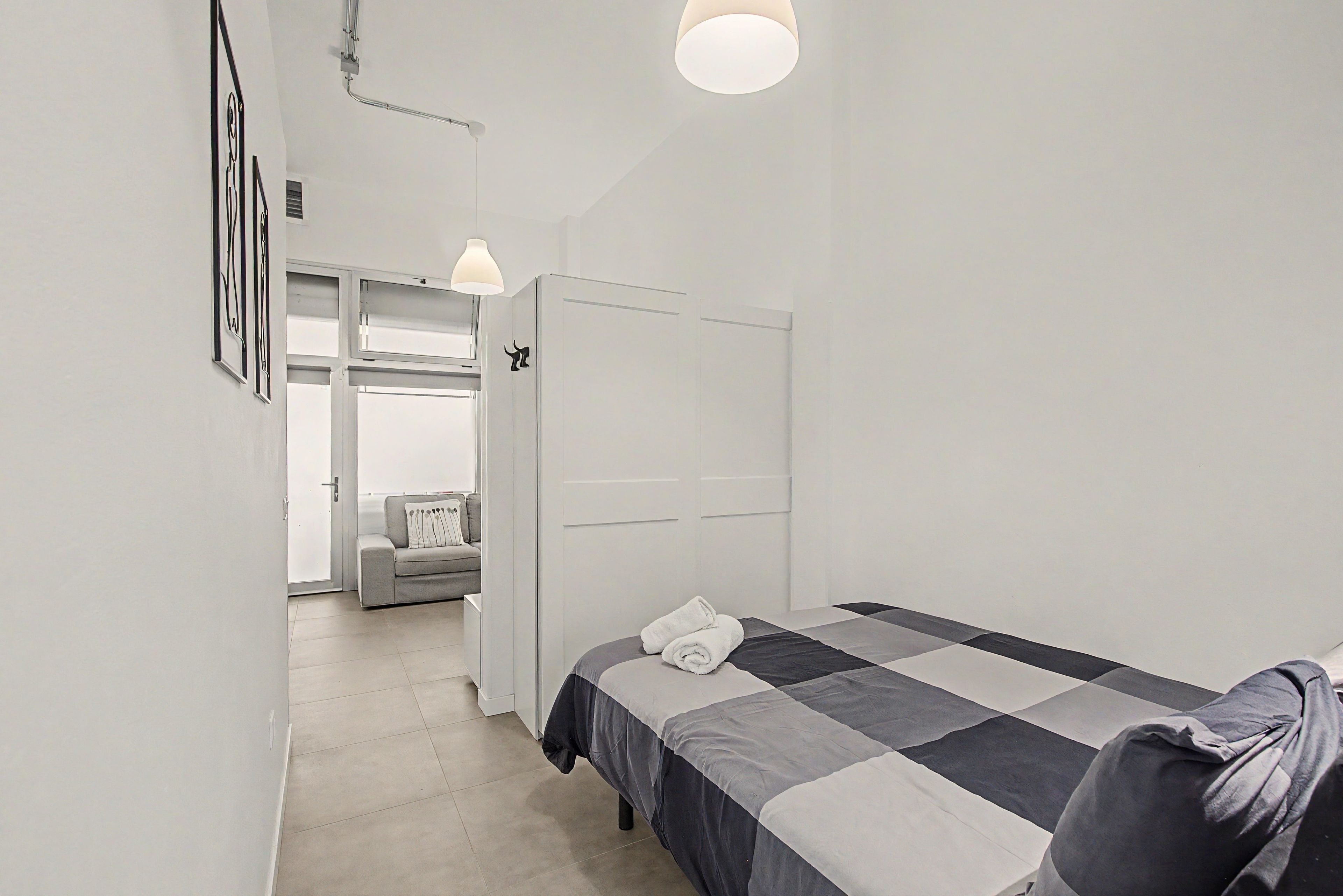 Un dormitorio con cama, armario, puerta que da a otra habitación y lámpara colgante.