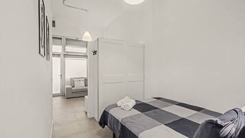 Un dormitorio con cama, armario, puerta que da a otra habitación y lámpara colgante.