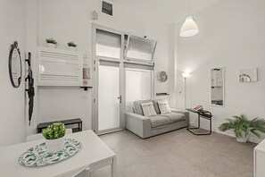 Ein schlicht eingerichtetes Wohnzimmer mit einer Couch, einem Esstisch und einer Pendelleuchte.