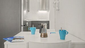 Un baño moderno con un lavamanos blanco, una cafetera y dos tazas azules sobre una mesa blanca.