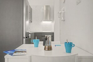 Ein modernes Badezimmer mit einem weißen Waschbecken, einer Kaffeemaschine und zwei blauen Tassen auf einem weißen Tisch.