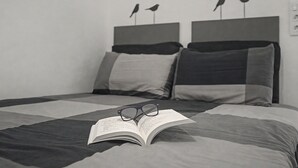 Una cama con un libro, lentes y un almohadón, y un cabecero decorado con dos adornos de pájaros.