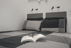 Ein Bett mit Buch und Brille darauf, ein Kopfkissen und ein Kopfteil mit zwei Vogelornamenten.