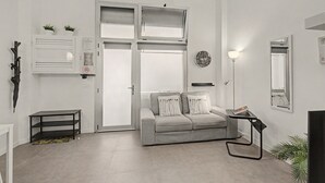Una sala de estar moderna con un sofá gris, una mesita auxiliar, una lámpara de pie y un ventanal grande.