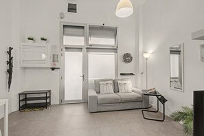 Ein modernes Wohnzimmer mit einem grauen Sofa, einem kleinen Beistelltisch, einer Stehlampe und einem großen Fenster.