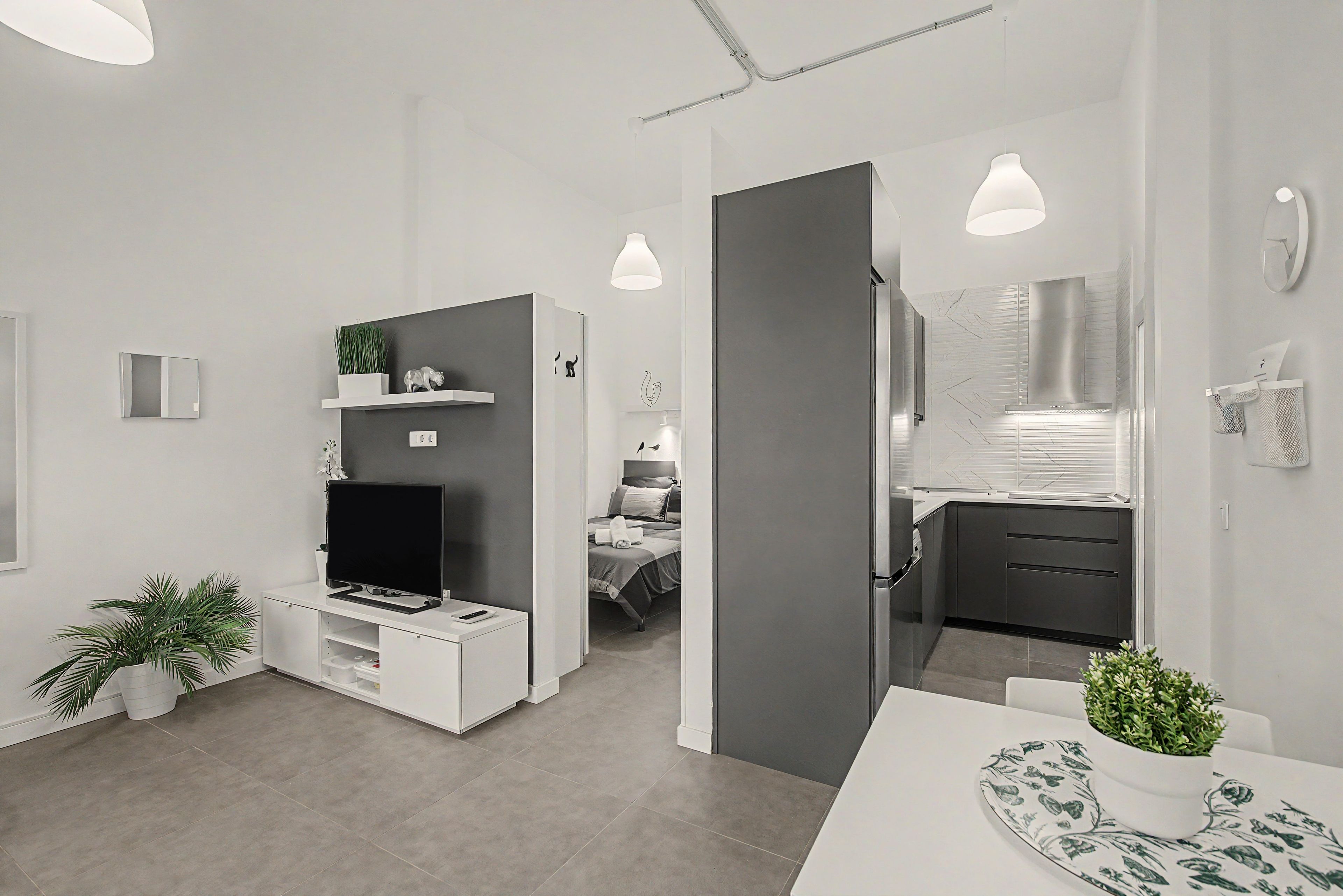 Un espace de vie moderne et minimaliste, doté d’un téléviseur à écran plat, d’une petite plante et d’un coin repas avec une table et des chaises.