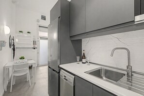 Eine moderne Küche mit eingebautem Geschirrspüler, Edelstahlgeräten, einer Marmor-Spritzschutzwand und einem minimalistischen Design.