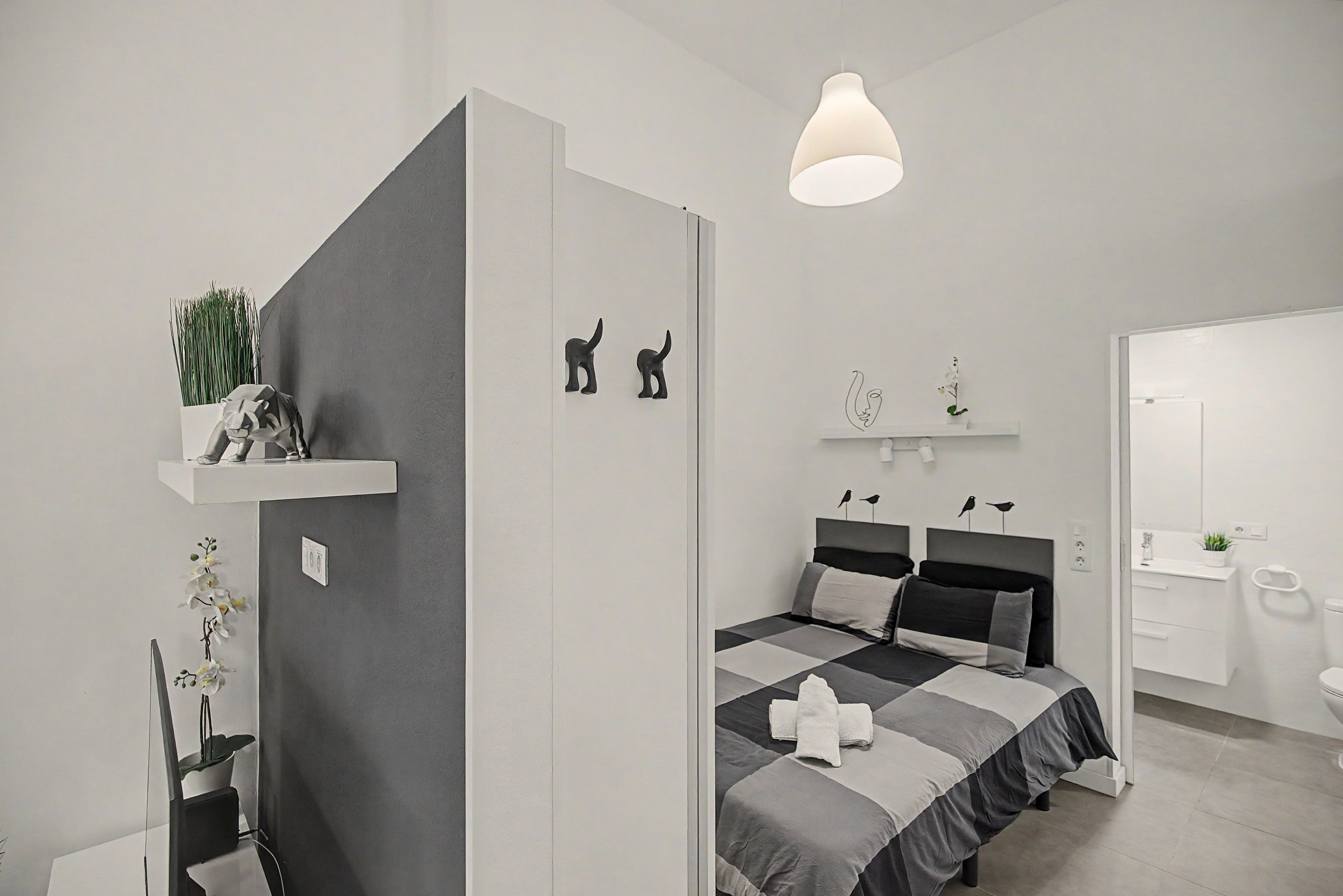 Une chambre à coucher moderne avec un lit, des tables de chevet, un luminaire suspendu et une petite plante posée sur une étagère.