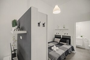 Ein modernes Schlafzimmer mit Bett, Nachttischen, einer Pendelleuchte und einer kleinen Pflanze auf einem Regal.