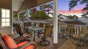 En overdækket terrasse med et bord og stole, udsigt til kvarteret og en solnedgang i baggrunden.