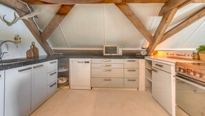 A kitchen with a sloped ceiling, wooden beams, a microwave, and a stove. - Cozy Stay With Recreation Room (Doorn)
