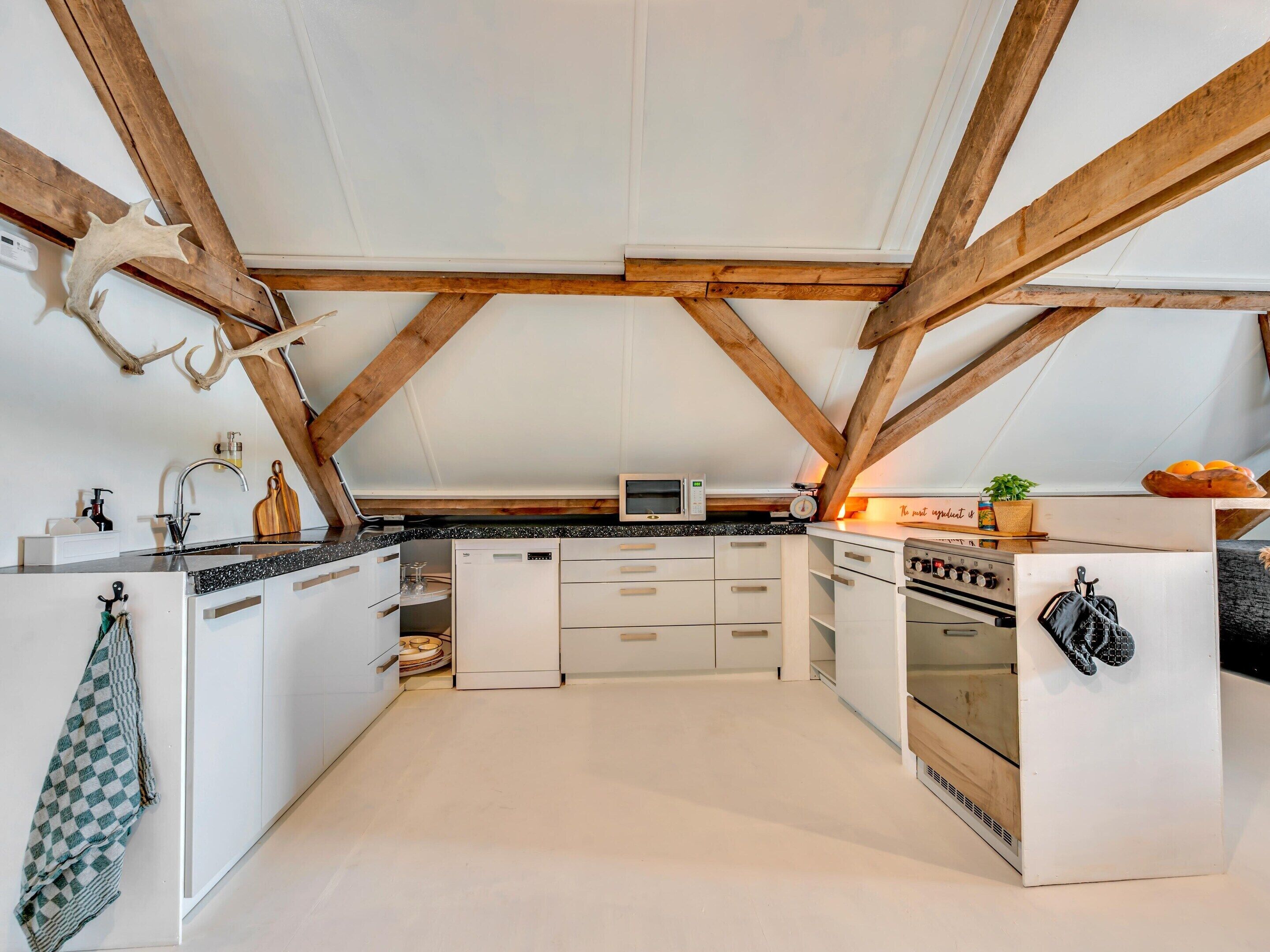 A kitchen with white cabinets, a microwave, an oven, and a wooden ceiling with exposed beams.