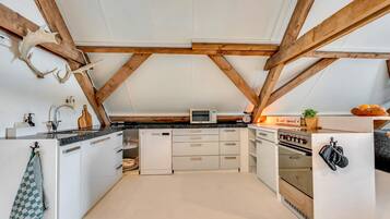 A kitchen with white cabinets, a microwave, an oven, and a wooden ceiling with exposed beams.