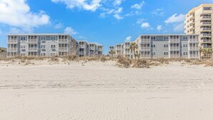 Ett hotell vid stranden med flera våningar, balkonger och en sandstrand på förgrunden.