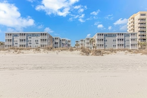 Ein Strandhotel mit mehrstöckigen Gebäuden, Balkonen und einem Sandstrand im Vordergrund.