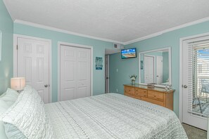 Ein Schlafzimmer mit Bett, Kommode, Fernseher und einer Tür.