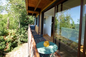 A balcony with a wooden deck, a table with a yellow object, and a glass door leading to a room. - Unique barn with a 100-square-meter terrace overlooking the Pyrenees (Auch)