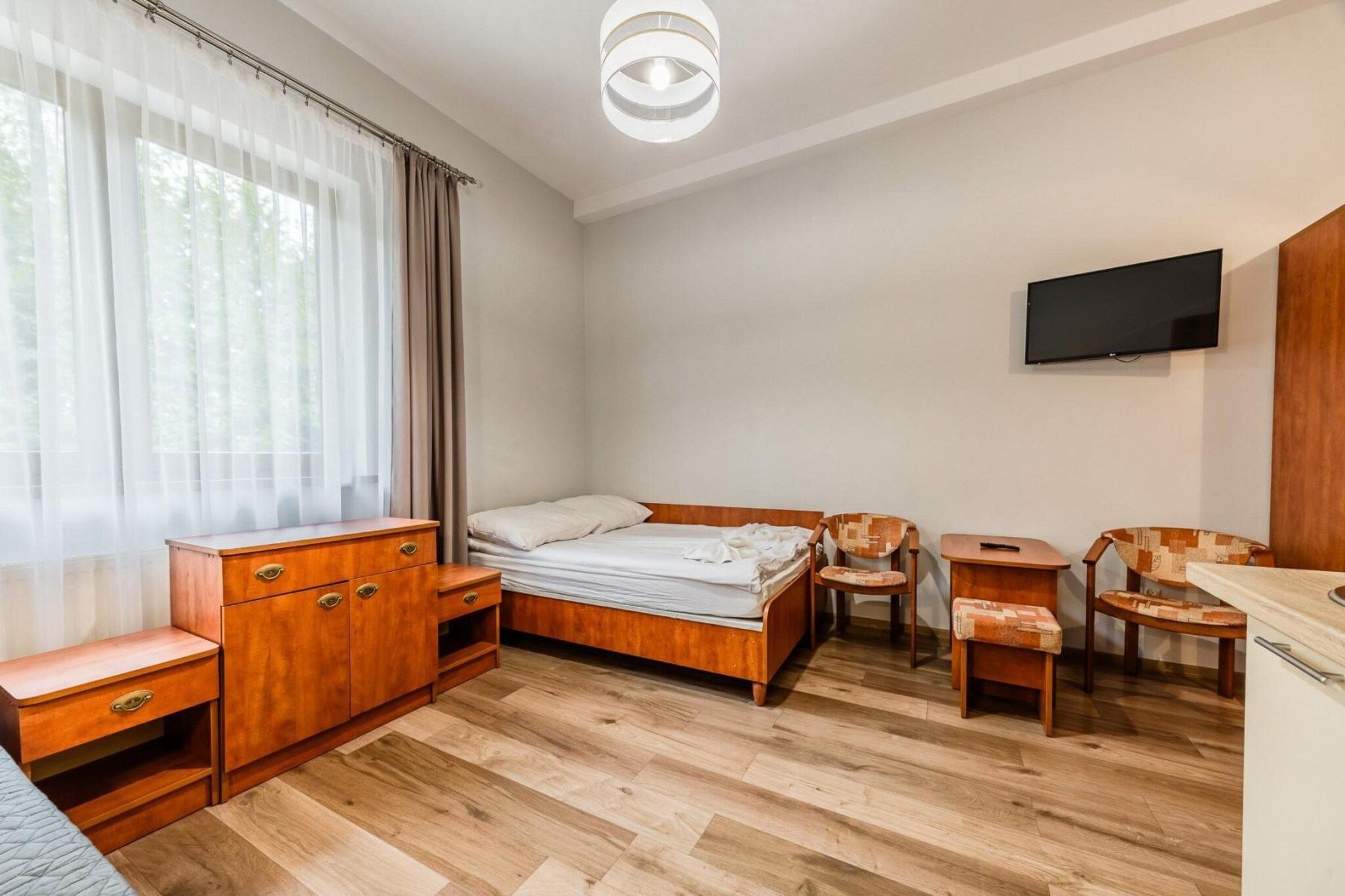 A bedroom with a bed, wooden furniture, a TV, and a window with curtains.