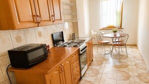 Een keuken met houten kastjes, een magnetron, fornuis en een eettafel met stoelen.