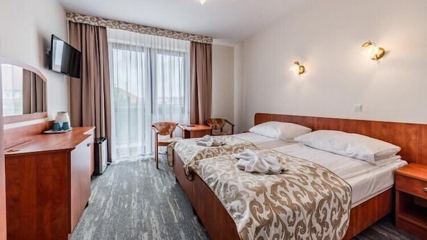 Een hotelkamer met een bed, een bureau, een stoel, een televisie en een raam met gordijnen.