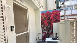Et lille udendørs siddeområde med en metalstol og et bord, en dør med et nummer på skiltet, og en væg med et blomster mural.