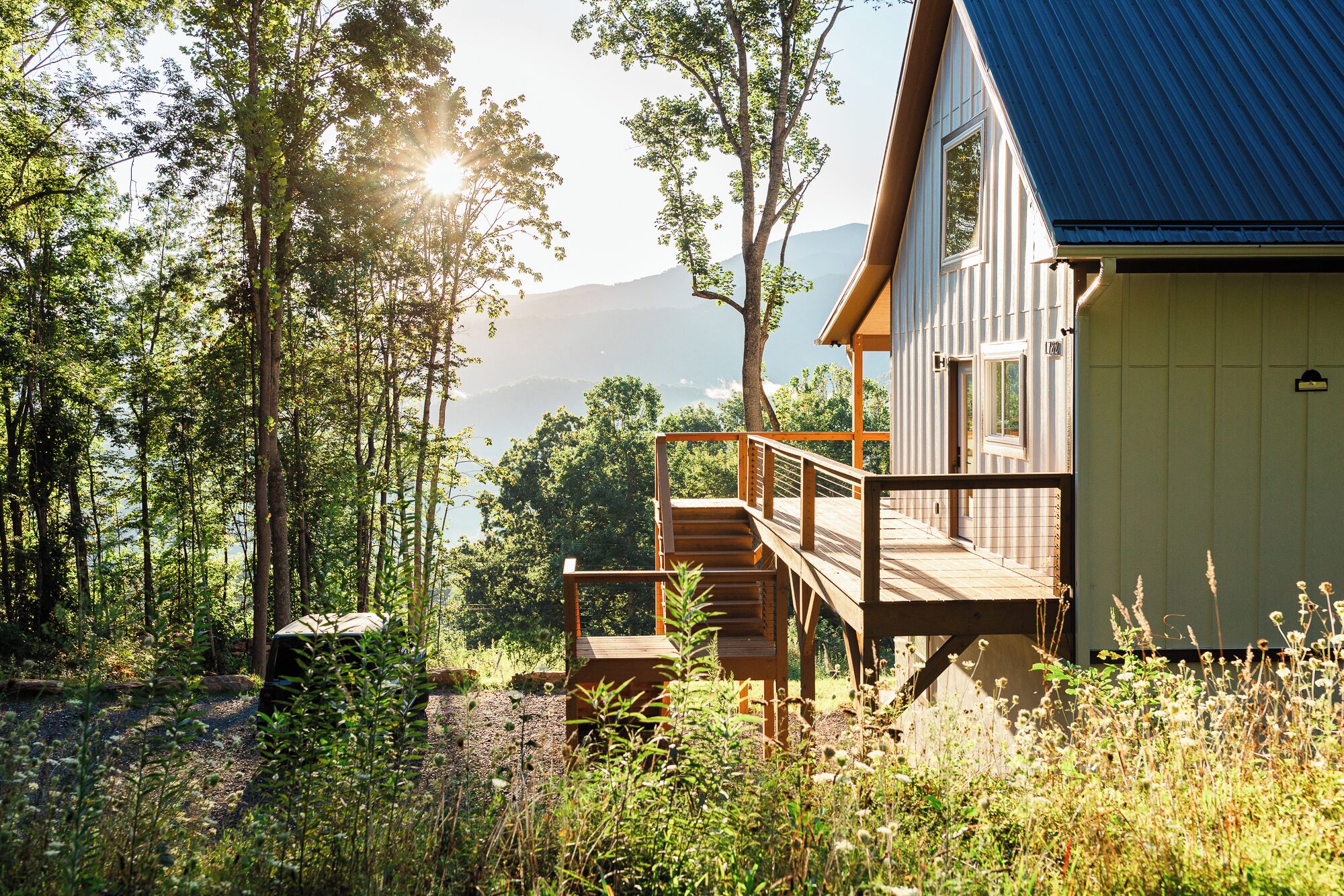 Een chalet met een houten terras en uitzicht op bos en bergen.