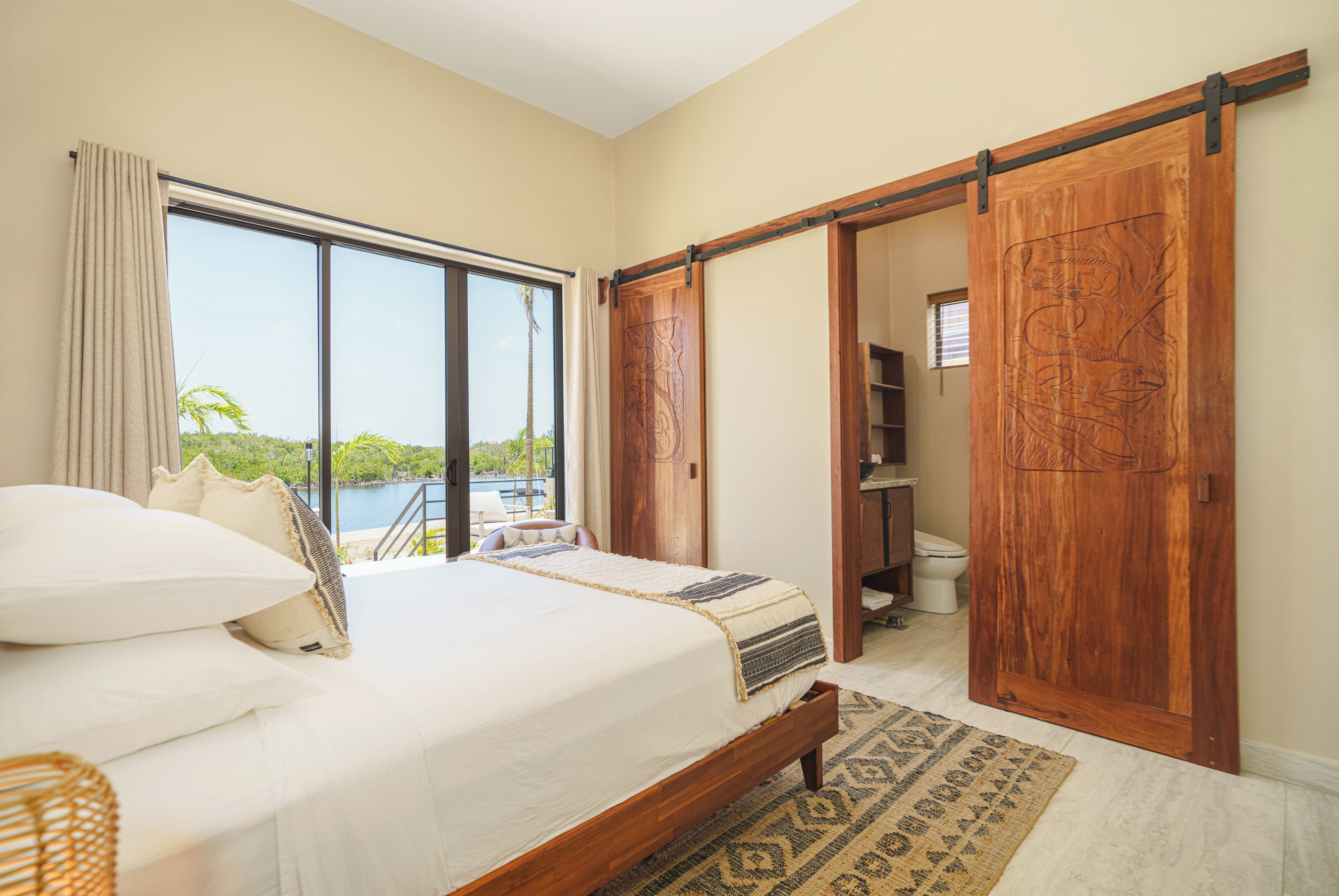 A bedroom with a large bed, a view of a body of water, and a sliding door leading to a bathroom.