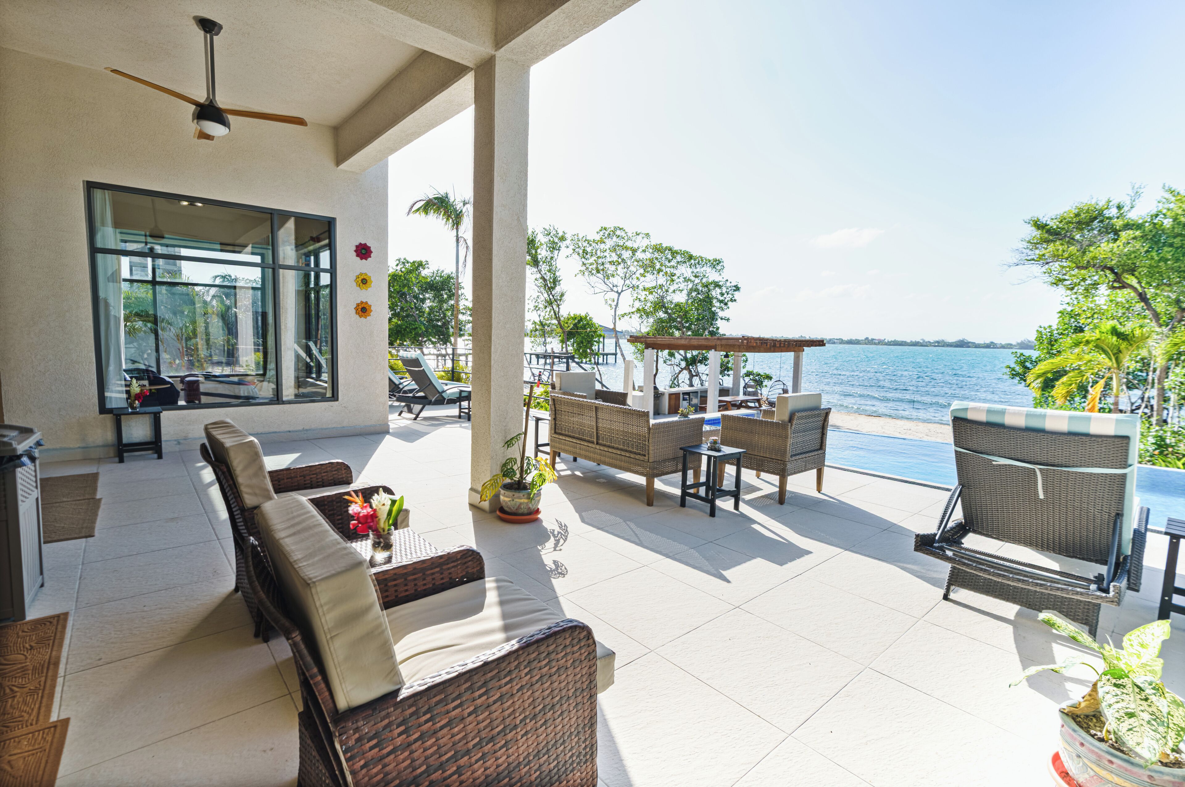 A covered outdoor seating area with wicker furniture, a ceiling fan, and a view of the sea.