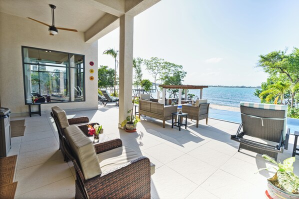 A covered outdoor seating area with wicker furniture, a ceiling fan, and a view of the sea.