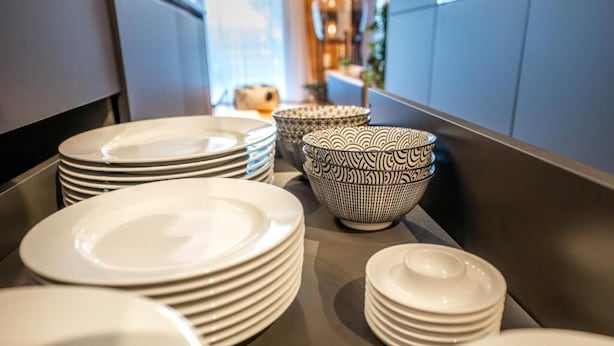 A kitchen counter with stacks of white plates and bowls, some with patterns.