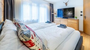 A hotel room with two beds, a television, a mounted deer head, and a large window with curtains.